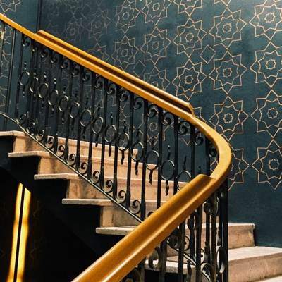 a staircase with yellow handles infront of a wall with blue and gold pattern wallpaper